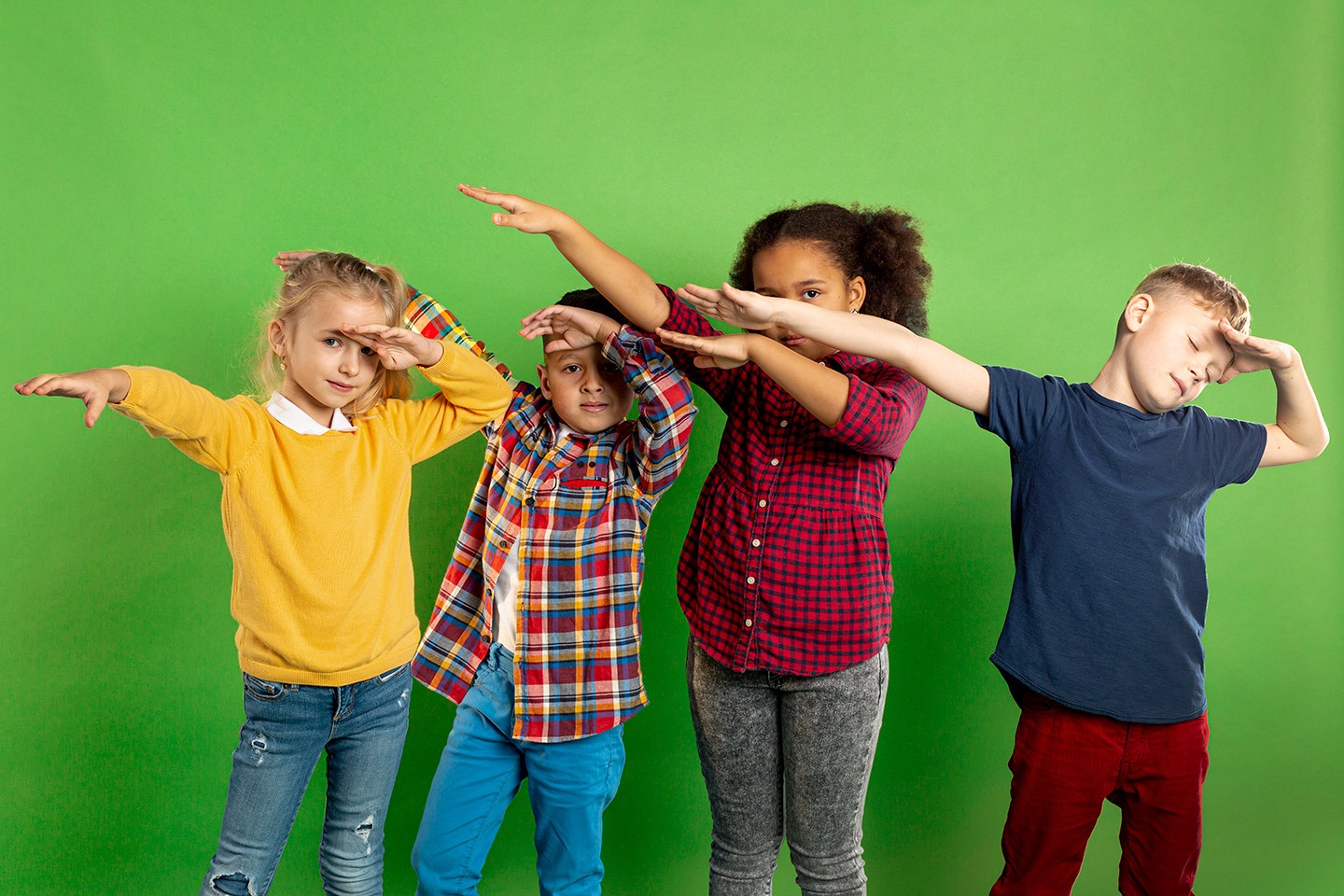10 Gründe für Tanzen in der Grundschule / Primarstufe Vier fröhliche Grundschulkinder machen Tanzbewegungen und posieren vor einem grünen Hintergrund – 10 Gründe, warum Tanzen in der Primarstufe wichtig ist.