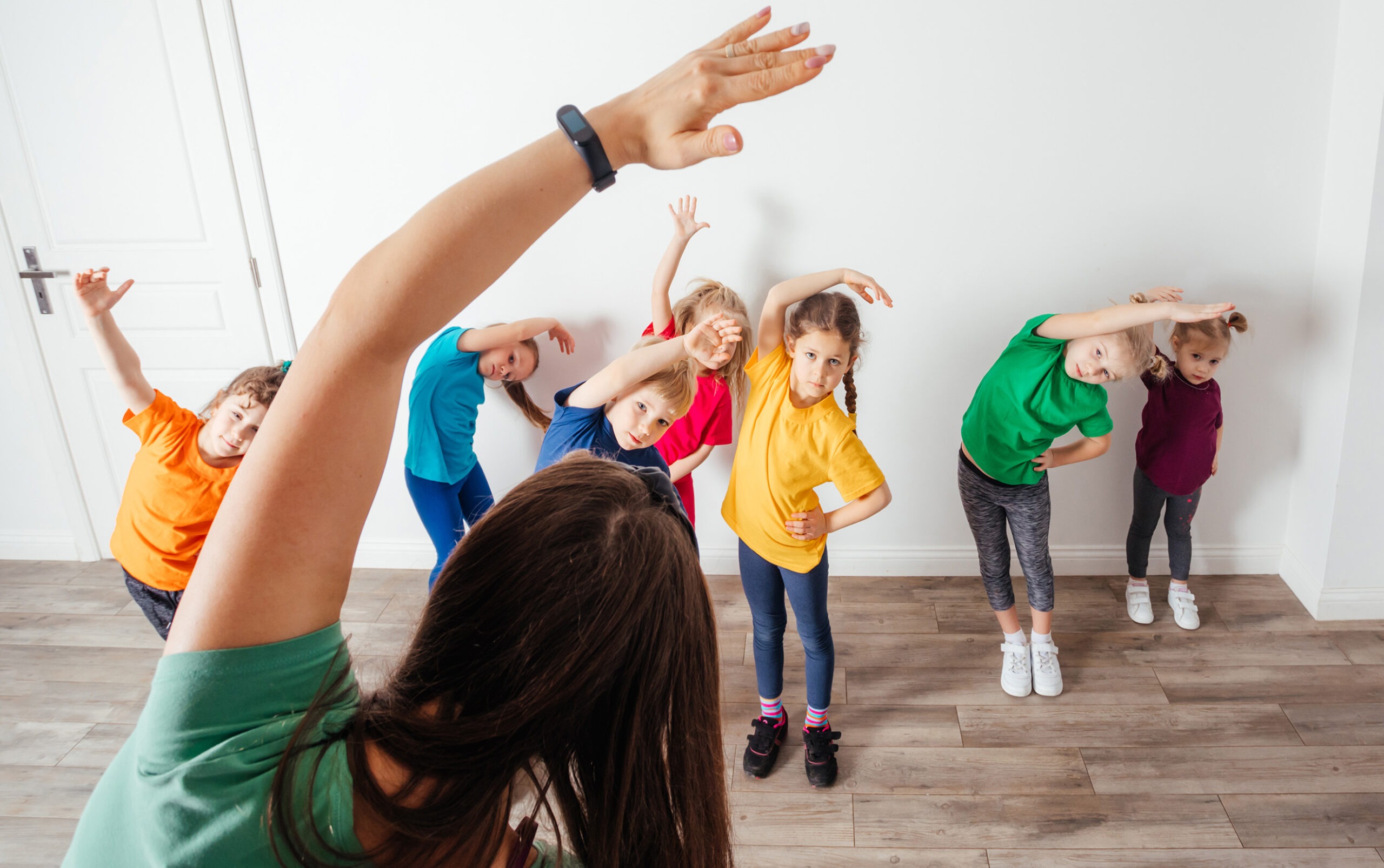 Spiegeltanz in der Grundschule: Methodik und Tipps Eine Lehrerin zeigt Kindern in der Grundschule eine Dehnübung – Perspektive auf Spiegeltanz und methodische Vermittlung von Bewegungen.