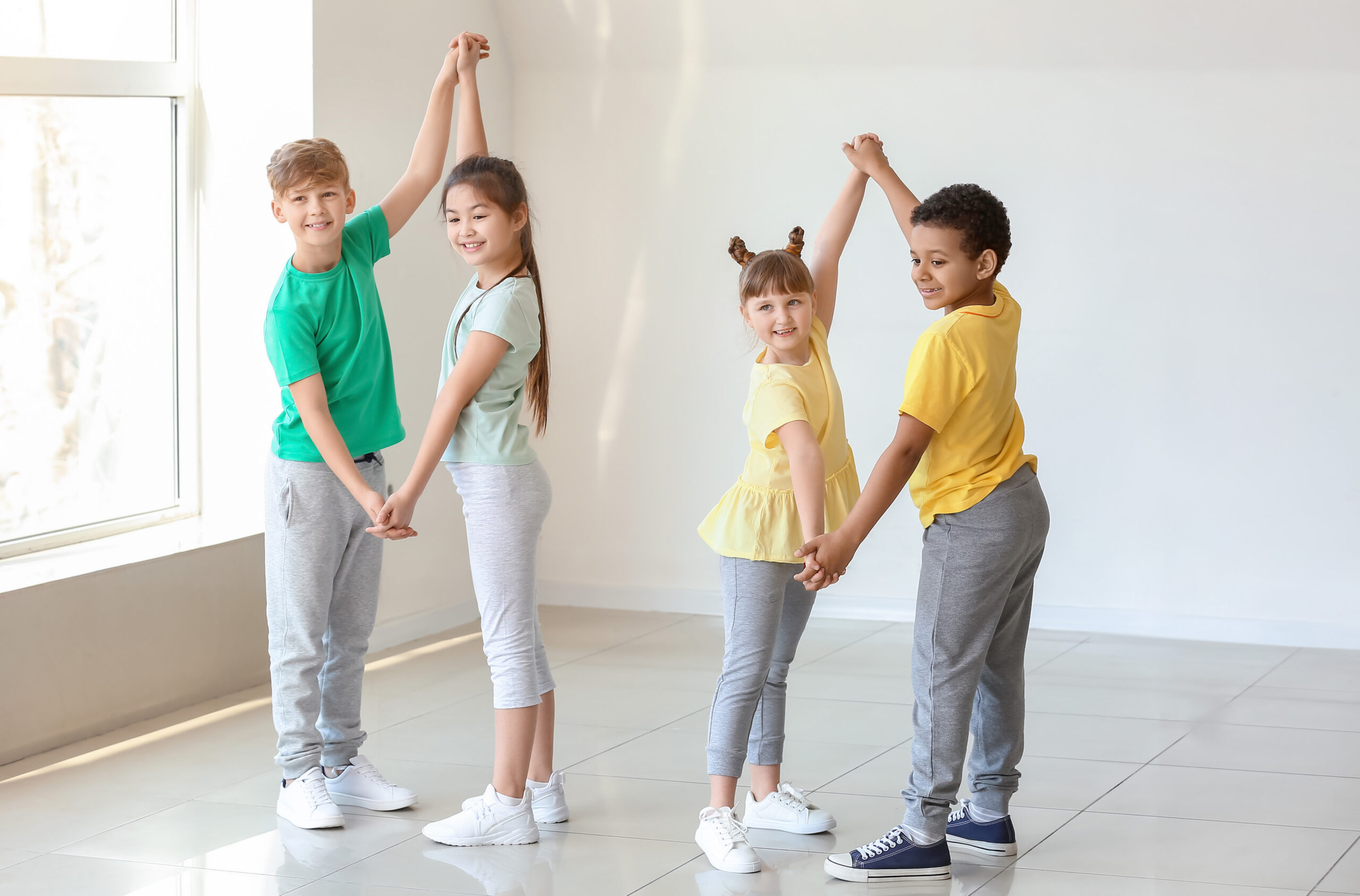 Tanz im Sportunterricht – Lehrplan Österreich Vier Schulkinder tanzen gemeinsam im hellen Turnsaal – Tanz als Teil des Sportunterrichts nach dem österreichischen Lehrplan.