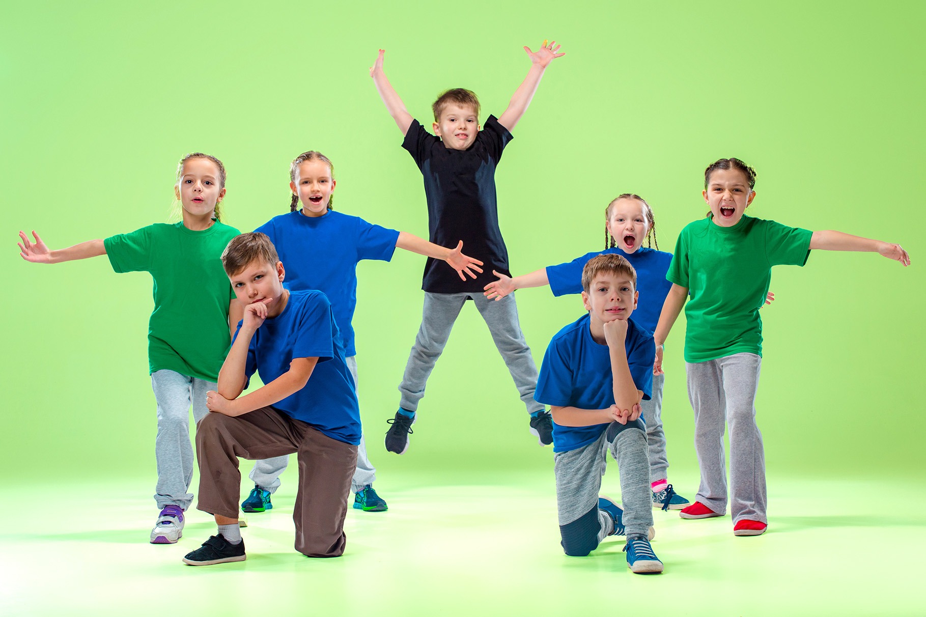 Eine Gruppe von Kindern zeigt verschiedene Tanzposen wie Springen und Balancieren zur Förderung der Grobmotorik.