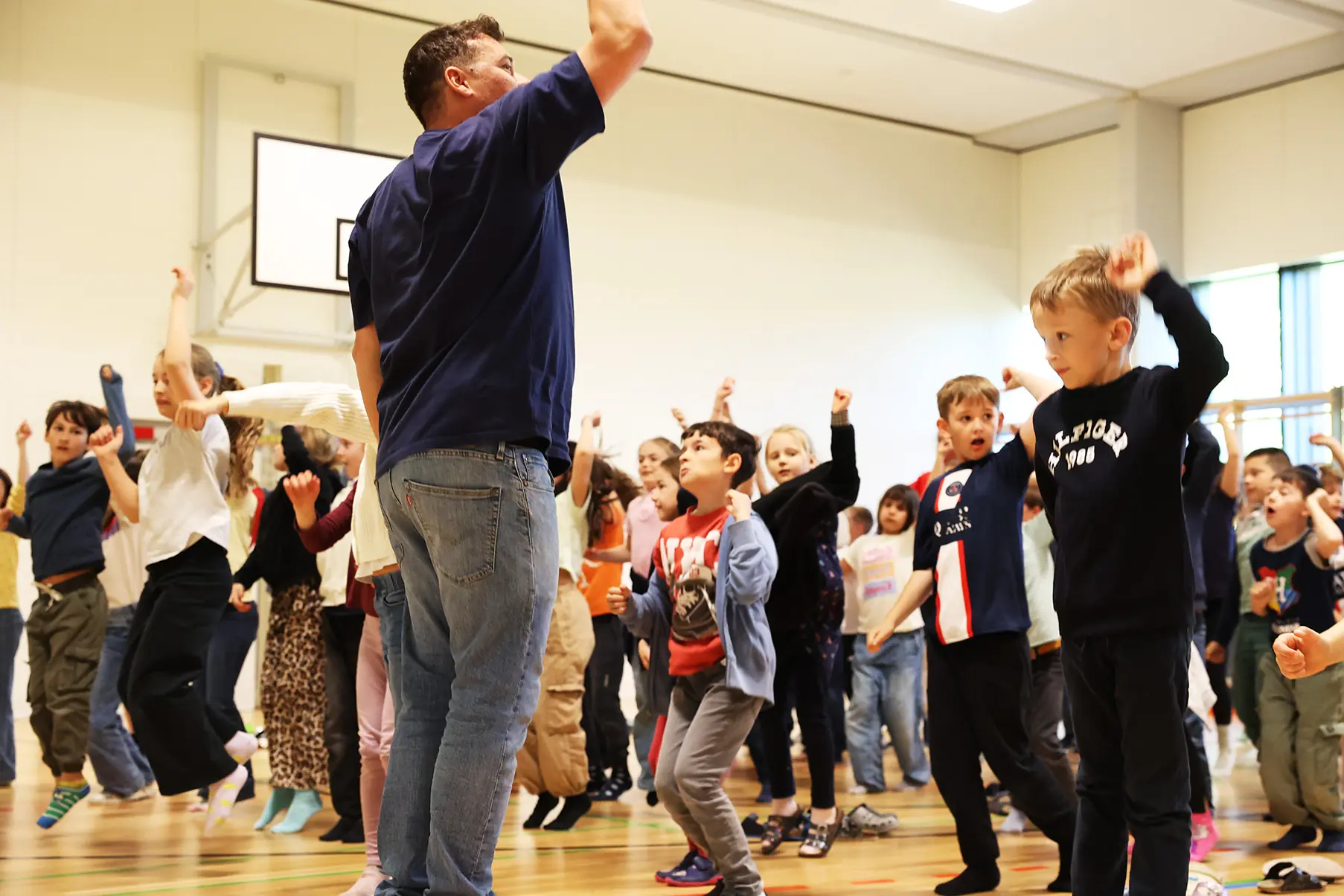 Die Spiegel-Methode: Intuitives Lernen im Tanzunterricht Eine Lehrkraft steht frontal vor einer Gruppe von Schulkindern in der Turnhalle und leitet einen Spiegeltanz an – direkte Nachahmung von Bewegungen.