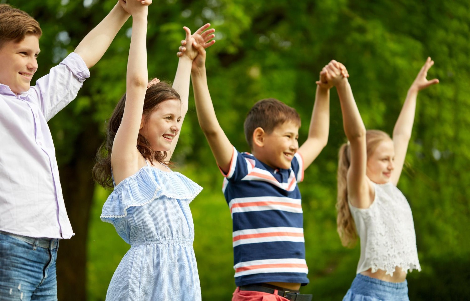 Geteilte Intentionalität & Synchronisation bei Kindern | groove2grow Vier glückliche Schulkinder halten im Freien die Hände hoch und zeigen soziale Synchronisation und Shared Intentionality im groove2grow Unterricht.