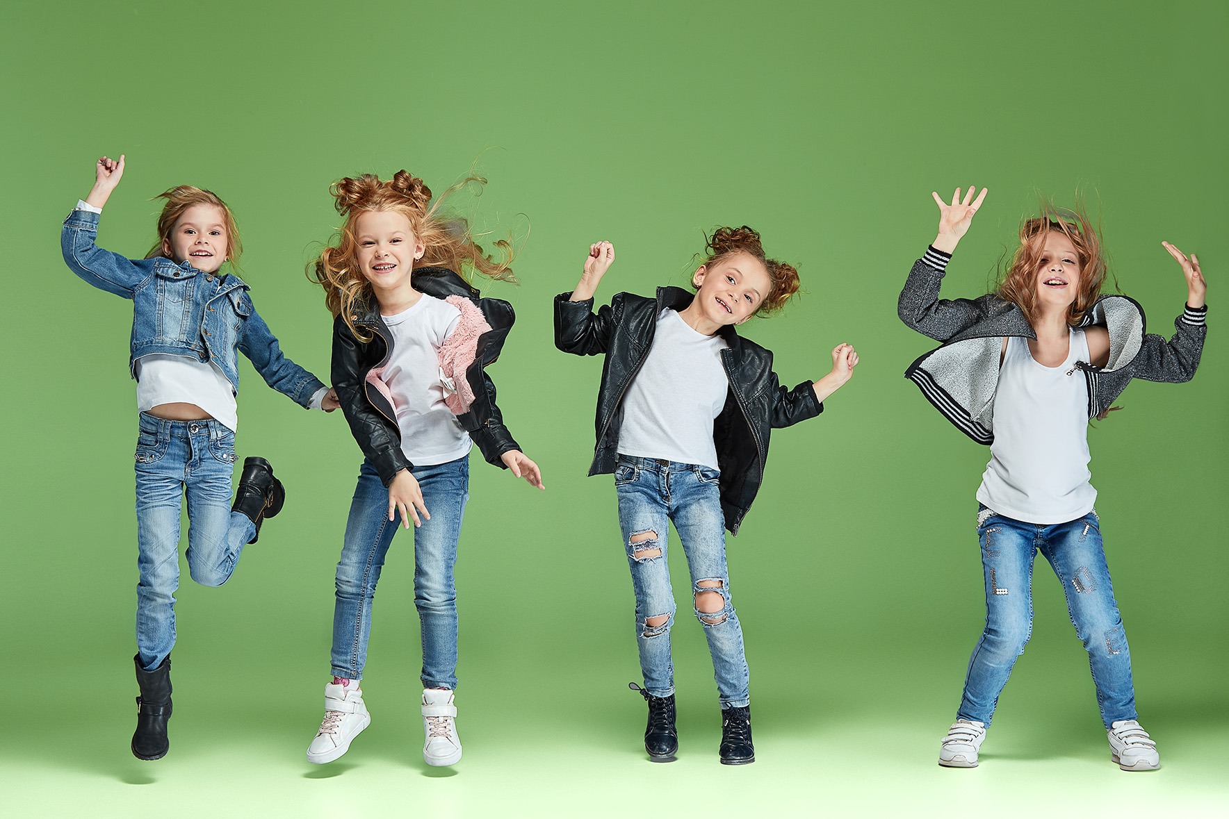 Vier begeisterte Kinder springen und tanzen voller Energie vor einem grünen Hintergrund – moderne Umsetzung von Tanz im Unterricht.
