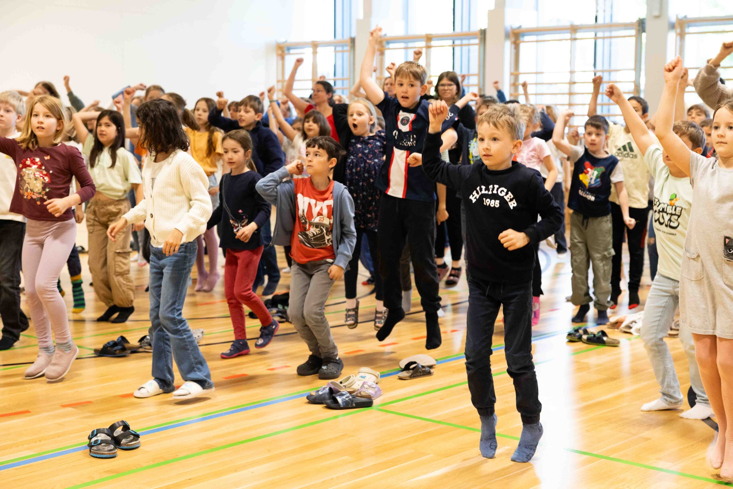 Bewegungsprojekt für die ganze Volksschule | groove2grow Eine ganze Volksschule springt und tanzt gemeinsam voller Energie in einer Turnhalle, um Synchronie und Kooperation durch das groove2grow Programm zu erleben.