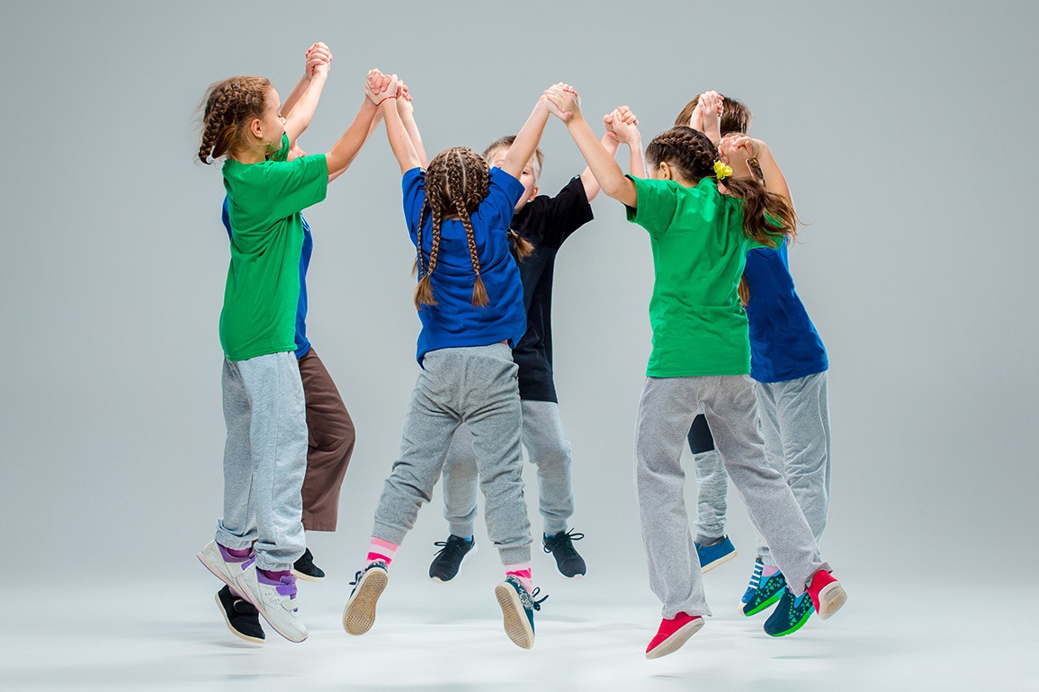 Eine Gruppe von Kindern tanzt im Kreis und hält sich an den Händen – Symbol für Teamarbeit und soziale Interaktion.