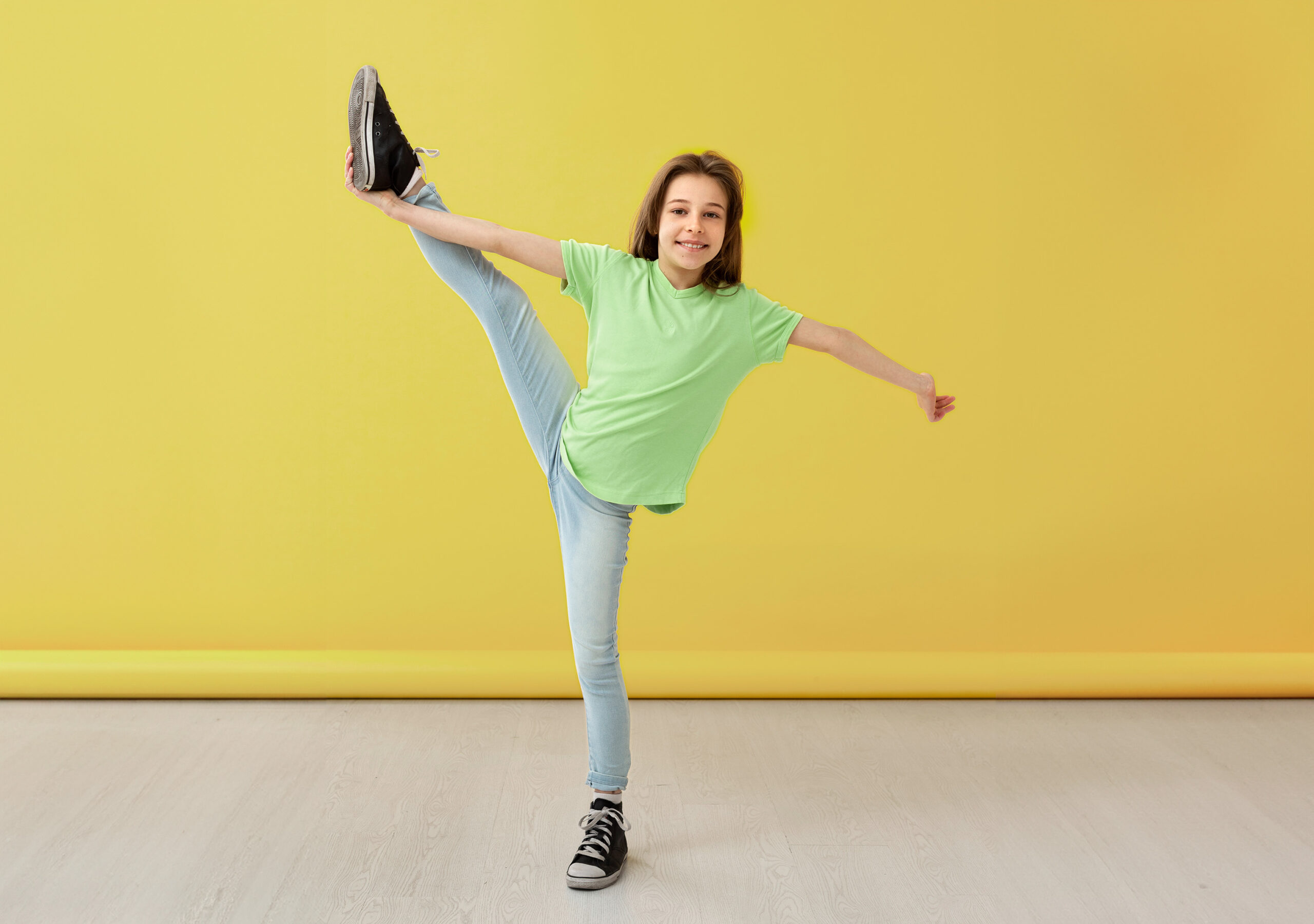 Ein Mädchen hält lächelnd eine vertikale Bein-Balance-Pose – Demonstration von guter Körperhaltung und Körperbewusstsein durch Tanz.