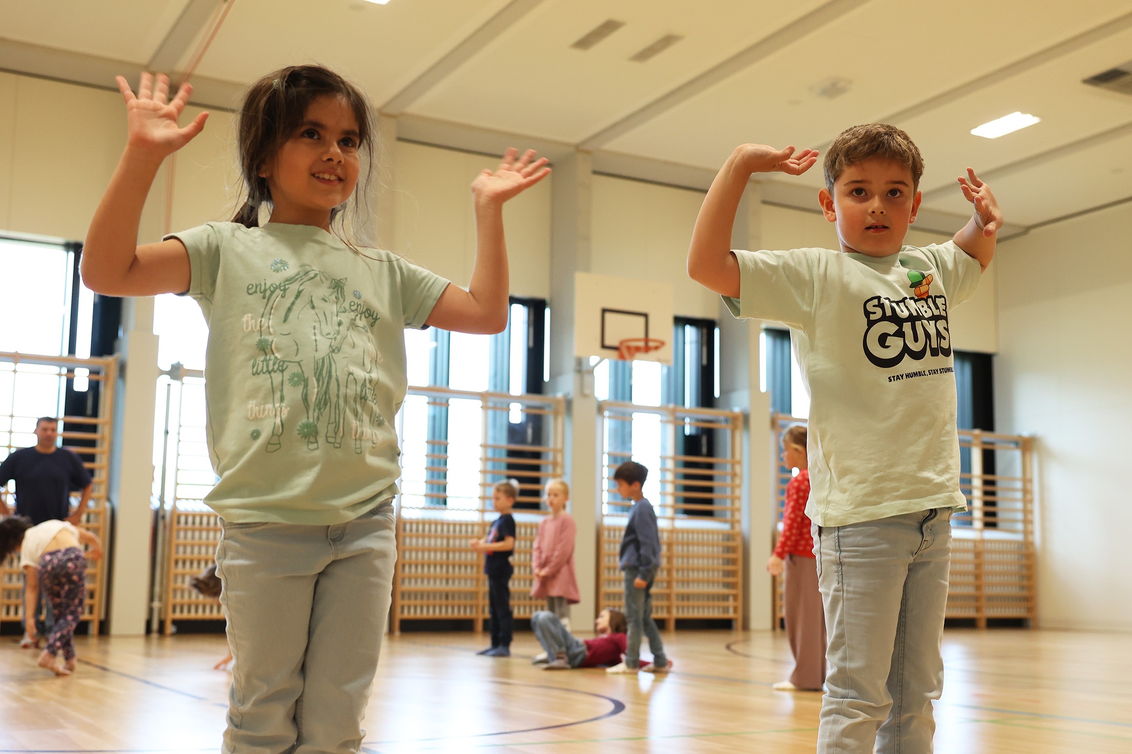 Zwei Kinder posieren selbstbewusst während einer Tanzeinheit in der Turnhalle – Ausdruck von individueller Identität und Freude an der Musik.
