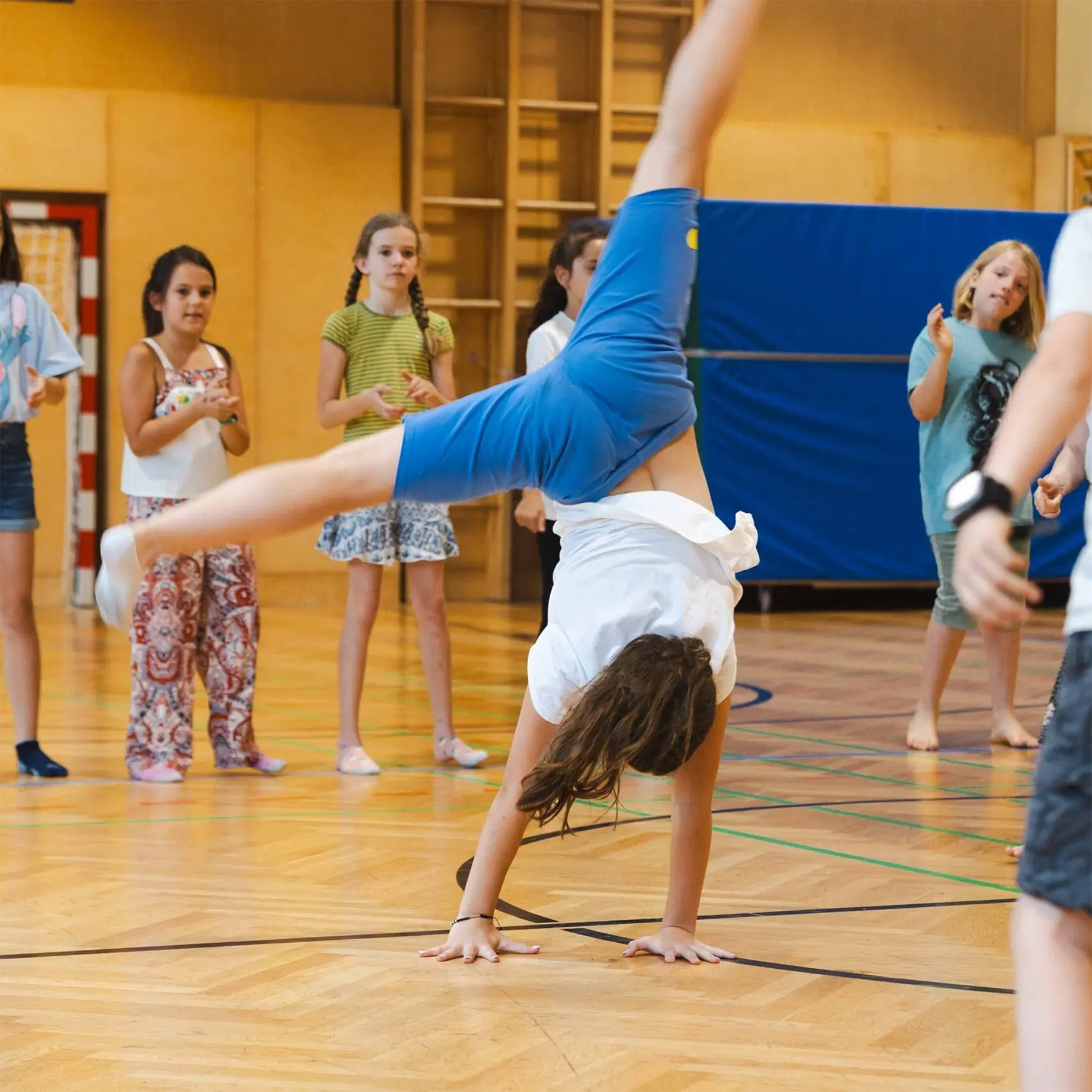 Ein Kind macht ein Rad in einer Turnhalle, während andere Kinder zusehen – inspiriert von der Soul Train Line.