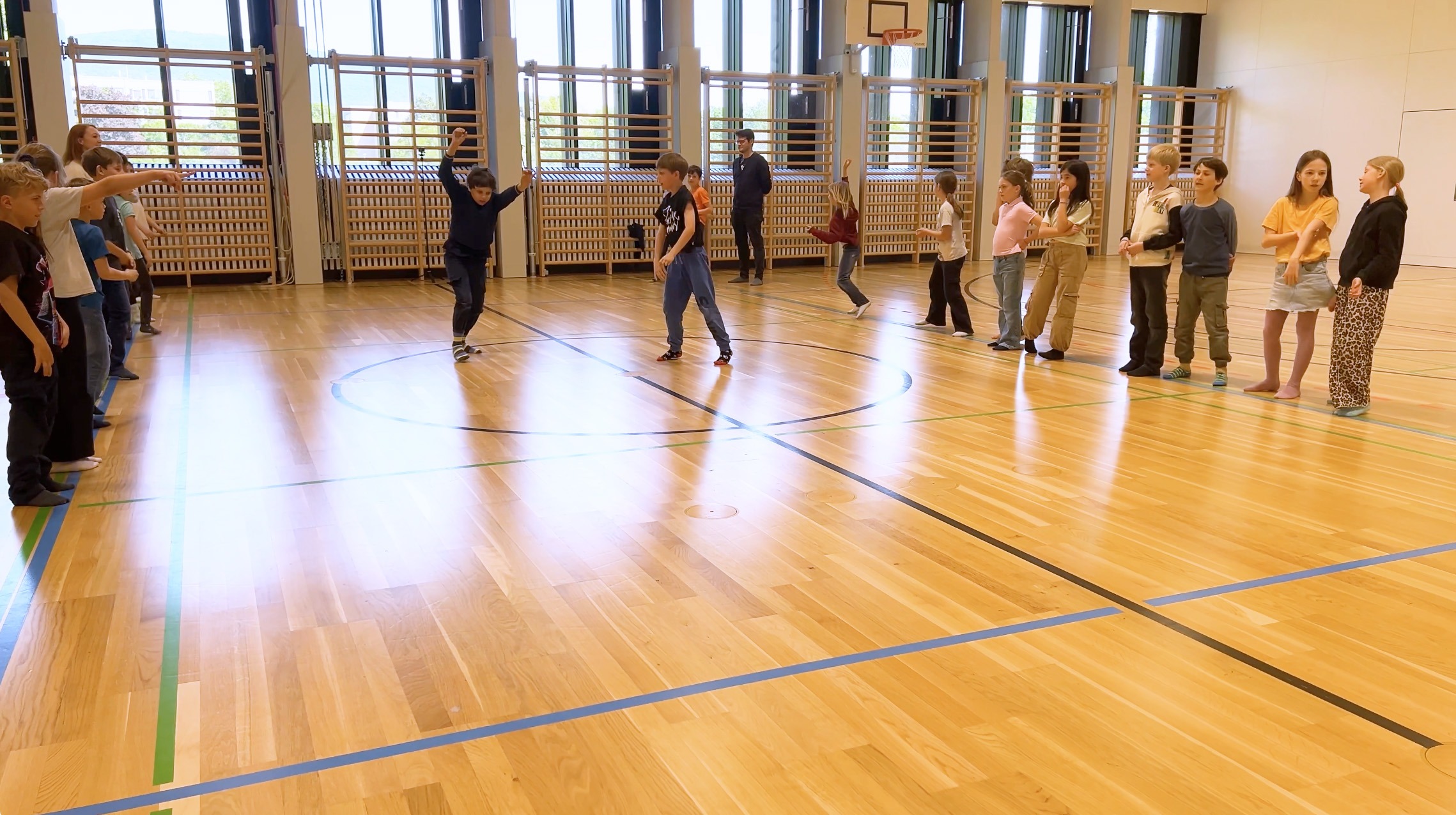 Schüler*innen bilden zwei Reihen in einer Turnhalle (Soul Train Line), während ein Junge in der Mitte tanzt und die Gruppe ihn anfeuert.